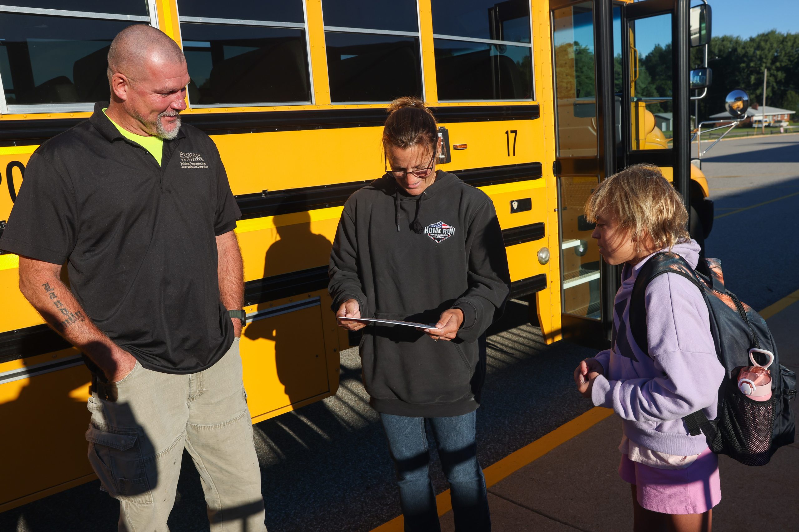 Three people standing in front of a school bus.